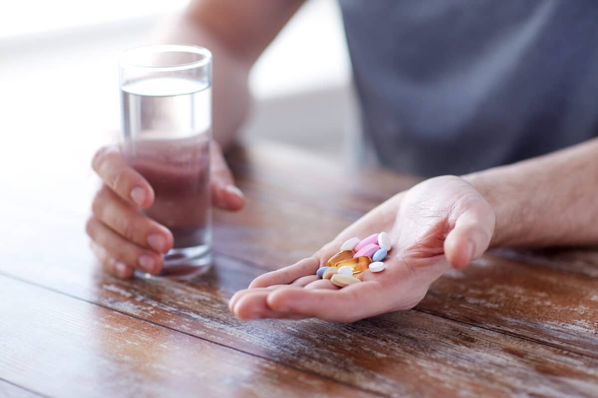 Person holding a lot of pills and a glass of water