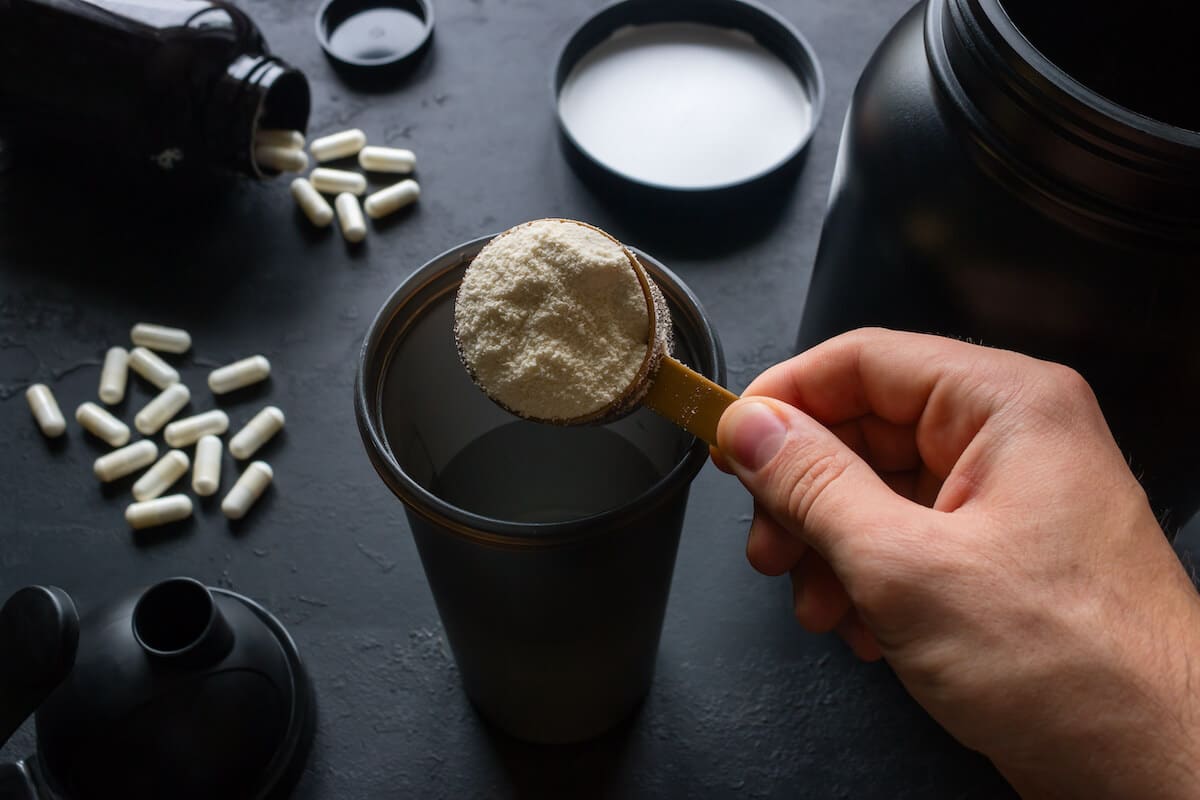 When to take amino acids: person preparing a protein shake, pills scattered in the background