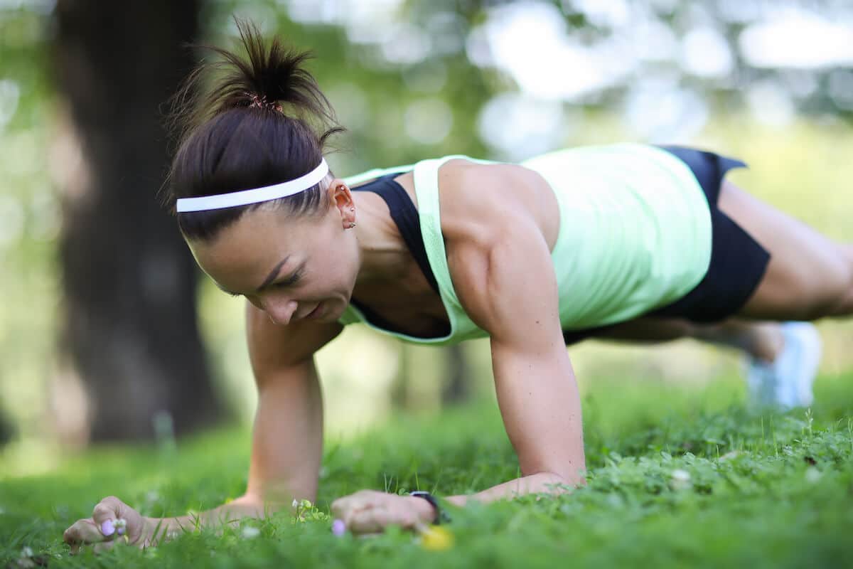 Calisthenics vs weights: woman doing a plank on her lawn