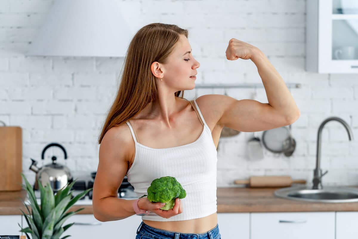 Vegan protein powder: woman holding a broccoli and flexing her muscles