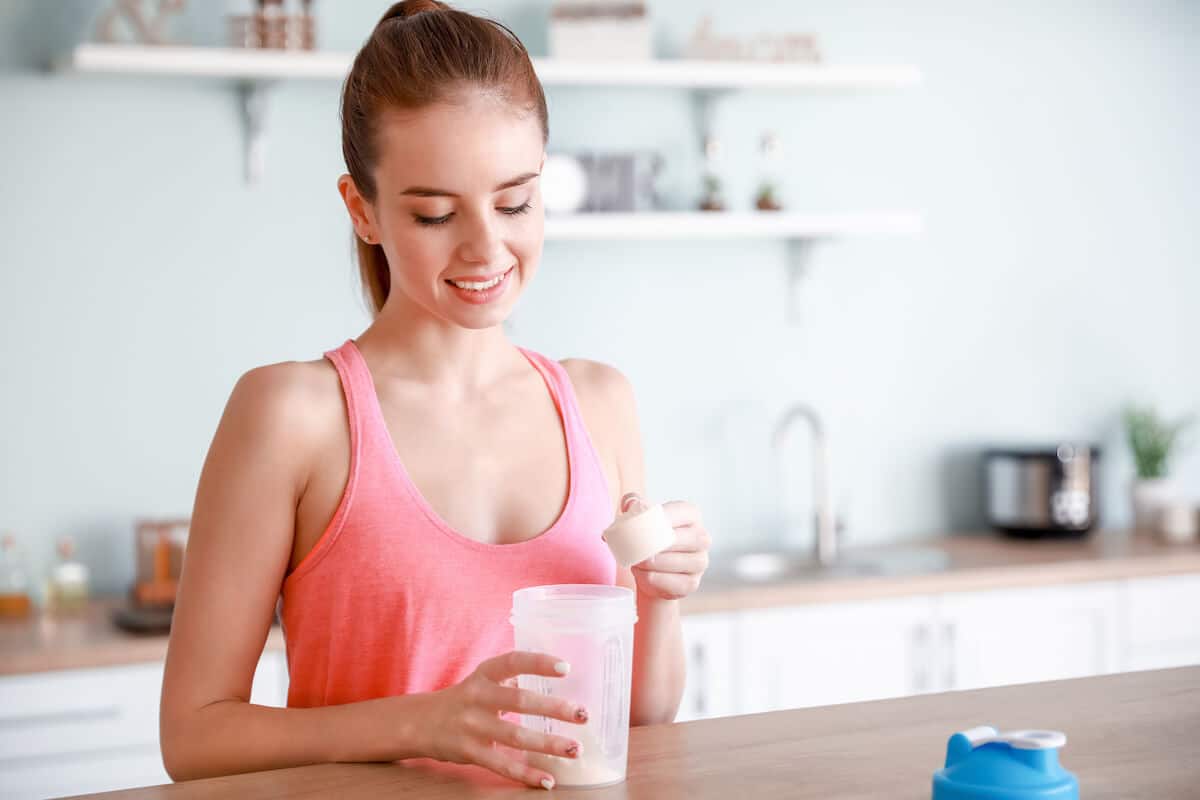 Protein before bed: woman pouring protein powder into her tumbler