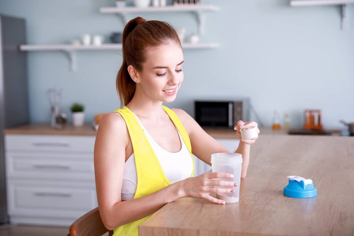 How is protein powder made: woman pouring protein powder into her tumbler