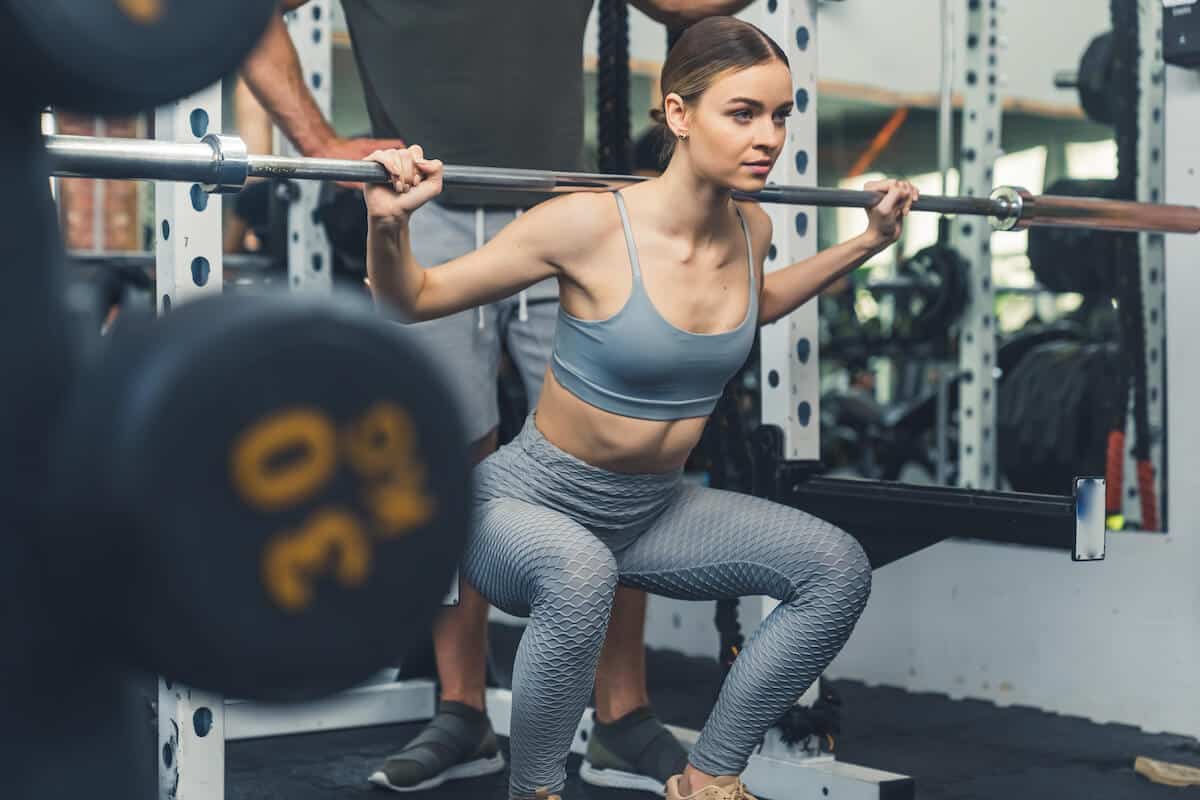 Best protein powder for sensitive stomach: woman doing some squats while lifting a barbell