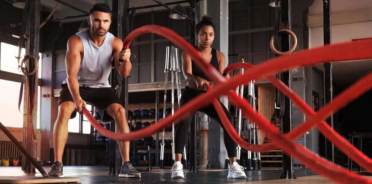 Should you drink protein shakes on rest days: man and woman working out using battle ropes