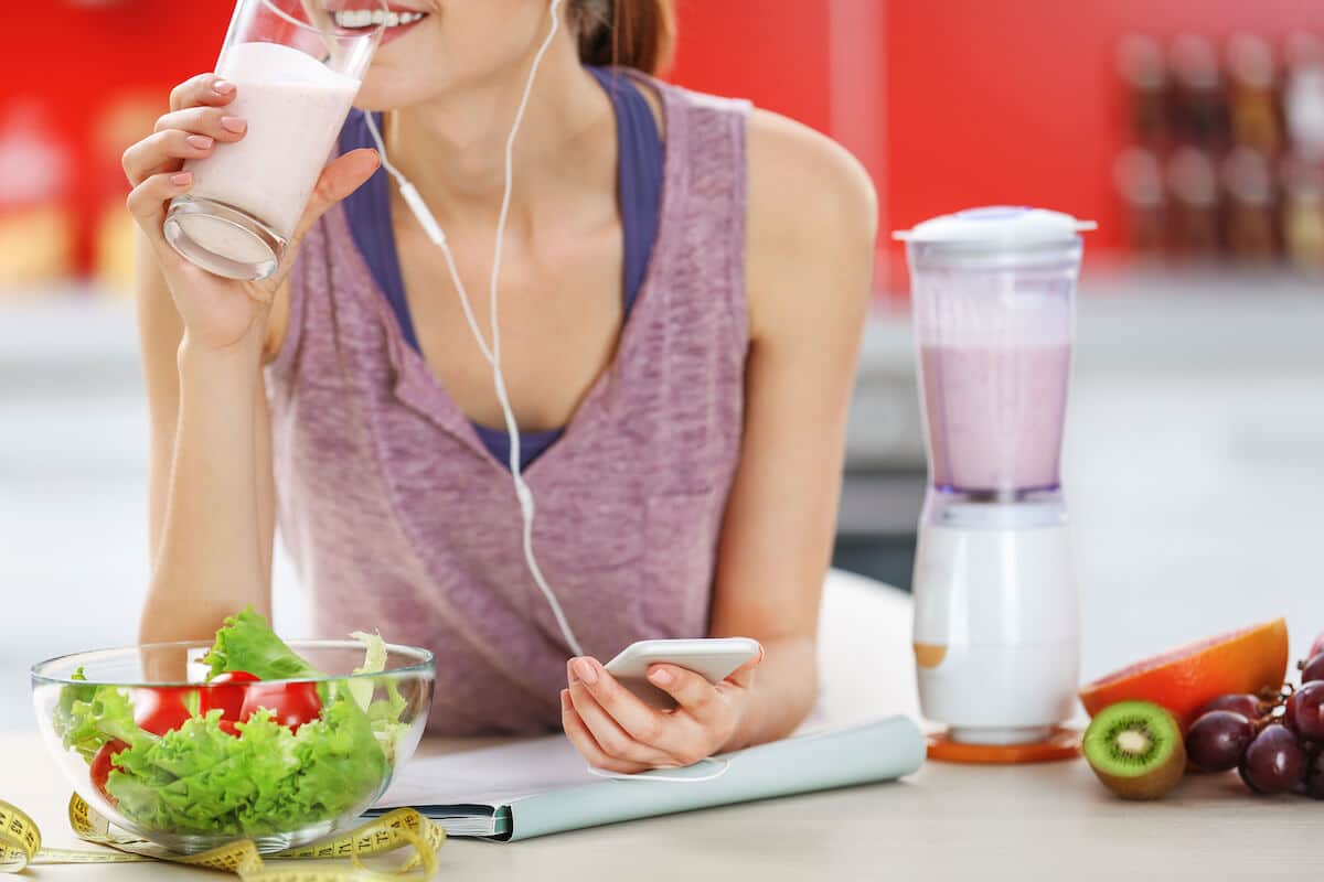 Metabolic confusion: woman drinking a healthy smoothie while holding her phone
